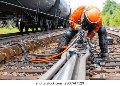 A worker in the process of a railroad track weld repair with a freight train passing