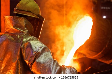 Worker In Protective Clothing Pouring Molten Metal In Foundry