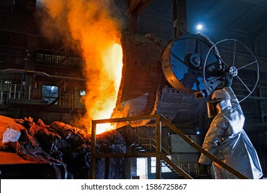 Worker In Protective Clothing Pouring Molten Metal In Foundry