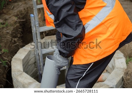 Worker in protective gear installing and inspecting septic system pipes inside a manhole at a private house, ensuring proper drainage, maintenance, and local wastewater management