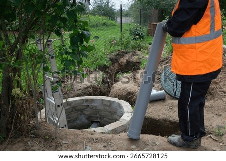 Worker in protective gear installing and inspecting septic system pipes inside a manhole at a private house, ensuring proper drainage, maintenance, and local wastewater management