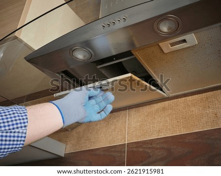 A worker in protective gloves opens a dirty kitchen hood grill. Maintenance and repair of household appliances.