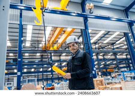 Worker with protective hard hat controlling an industrial crane with control remote