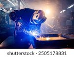 Worker with protective mask welding metal in workshop