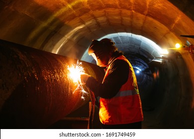 Worker in protective mask welding pipe in tunnel