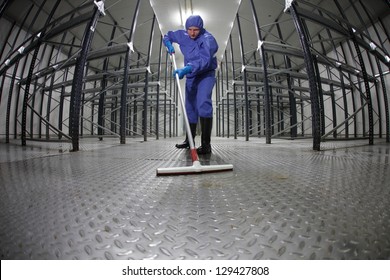 worker in protective overalls cleaning floor in empty storehouse - fish-eye lens
