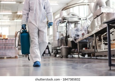 Worker In Protective Uniform Carrying Sprayer With Disinfectant And Walking Around Food Factory. Corona Virus Outbreak Concept.