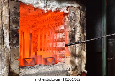 Worker pulls out the heated parts with tongs from an electric furnace for hardening metal. Dangerous work with high temperatures in heavy industry in a valve manufacturing plant