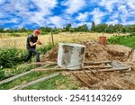 Worker pushes concrete ring along roller deck using crowbar lever.