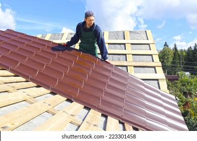 Worker puts the metal tiles on the roof of a wooden house - Shutterstock ID 223301458