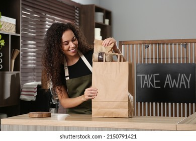 Worker putting coffee beans into paper bag at counter in cafe
