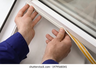 Worker putting rubber draught strip onto window indoors, closeup