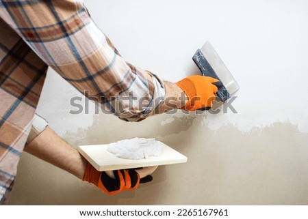 worker with putty knive near wall indoors, closeup. repair work of home. 