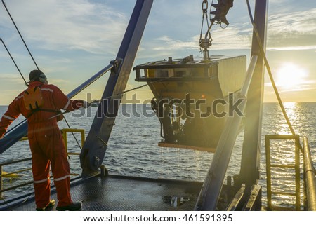 worker recovering robotics Remote Operated Vehicle (ROV) after entering sea surface during oil and gas pipeline inspection in the middle of South China Sea isolated on sunrise with glare