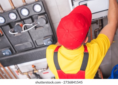 A worker in a red cap fixes a heating system in a utility room. Tools are nearby.