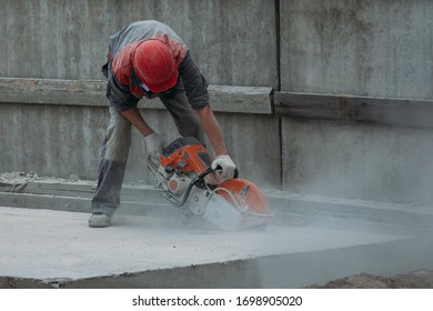 A Worker In A Red Helmet Is Sawing Concrete With A Large And Powerful Grinder