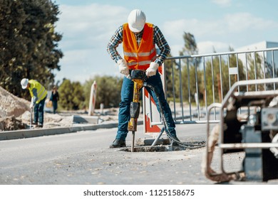 Worker in reflective vest and drill repairing street during roadworks