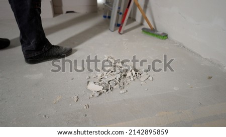 A worker removes construction debris with a brush. A man cleans up small debris at a construction site. Cleaning of premises from construction debris. Room cleaning and room cleaning. Collect construc