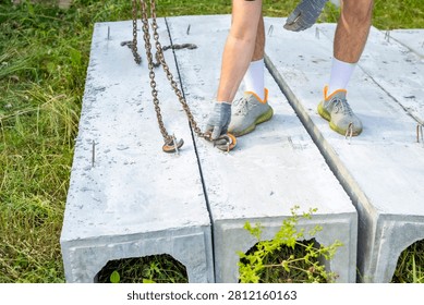 Worker removes lifting chains from precast concrete drainage channels on rural construction site. Drainage installation process