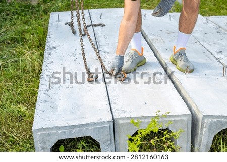 Worker removes lifting chains from precast concrete drainage channels on rural construction site. Drainage installation process