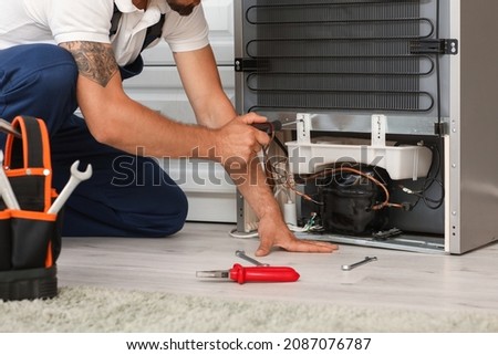 Worker repairing fridge in kitchen
