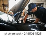 Worker, repairman wearing cap, repairing car engine. Hardworking man opening car hood, looking, working in garage, auto, servicing center. Concept of manual labor.