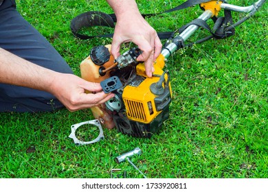 Worker Repairs A Carburetor In Trimmer Or Lawn Mower That Lies On The Grass