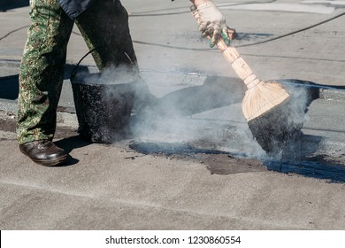 Worker Repairs The Roof With Molten Tar From A Bucket With A Broom. Roof Repair Tar.