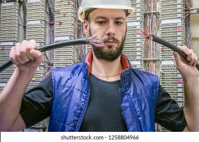  Worker Restores The Connection In The Data Center Server Room. Engineer In A Helmet Will Connect Damaged Internet Backbone Wire. Technician Holds In His Hands The Two Ends Of Torn Telephone Cable.