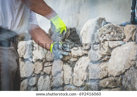 worker rides a stone wall on a traditional renovation site of NOIRMOUTIER, FRANCE