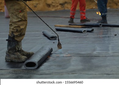 worker rolls a roll of bitumen coating on a construction site .