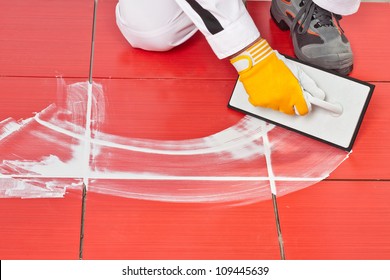 Worker With Rubber Trowel Applying White Grout On Red Tiles On Floor