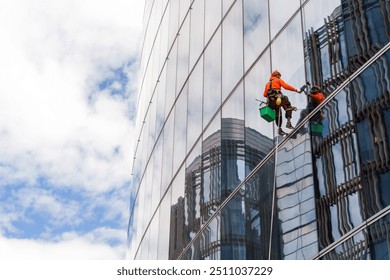 Worker in safety gear clean the windows of a tall glass building, suspended high above the ground. - Powered by Shutterstock