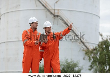 Worker in safety gear using tablet near industrial storage oil tanks refining petrochemical industry factory.