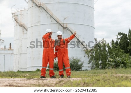 Worker in safety gear using tablet near industrial storage oil tanks refining petrochemical industry factory.