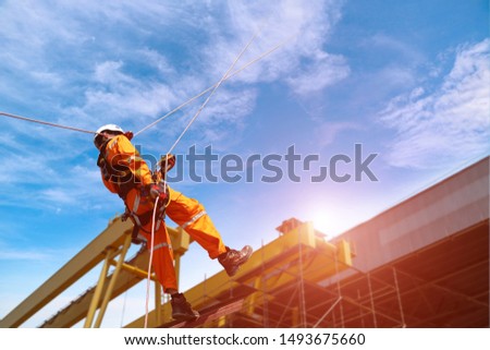 worker safety uniform, Rope access at construction wearing full safety body harness with helmet protection hanging upside on roof factory and crane background.