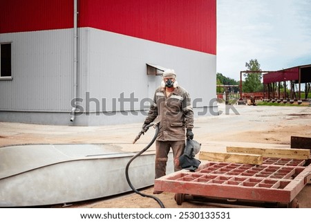 A worker is sandblasting a metal structure to effectively remove rust at an industrial plant, ensuring the surface is prepared for further treatment.