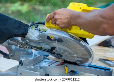 A worker is sawing a board on a yellow circular saw, a close-up shot, the photo was taken outdoors on a clear summer day