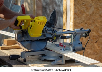 A worker is sawing a board on a yellow circular saw, a close-up shot, the photo was taken outdoors on a clear summer day