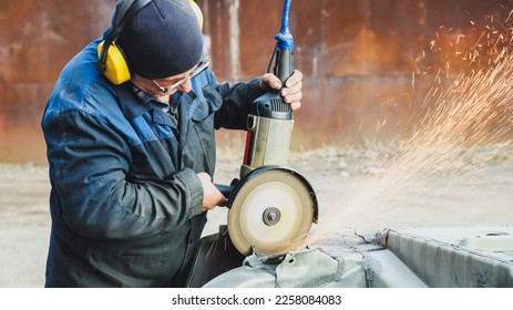 Worker saws metal with an old angle grinder. Selective focus. Outdoors. Flying sparks. Industrial concept - Shutterstock ID 2258084083