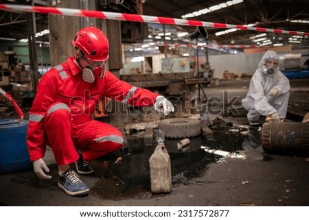 Worker or scientist industry wearing protective safety uniform, white glove and gas mask under cleaning up and lapping spilled oil in factory area to check in laboratory is industry safety concept.