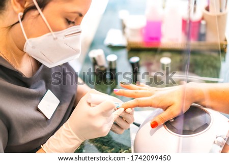A worker with security measures and a face mask painting colored nails of the client. Reopening after the corod-19 pandemic. Manicure and Pedicure Salon. Coronavirus
