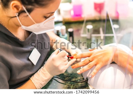 A worker with security measures and a face mask painting colored nails. Reopening after the corod-19 pandemic. Manicure and Pedicure Salon. Coronavirus