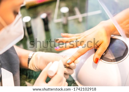 Worker with security measures and face mask painting colored nails of the client. Reopening after the corod-19 pandemic. Manicure and Pedicure Salon. Coronavirus