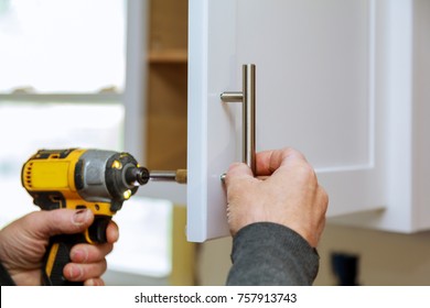 The Worker Sets A New Handle On The White Cabinet With A Screwdriver Installing Kitchen Cabinets