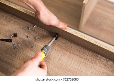 The worker sets a new handle on the white cabinet with a screwdriver - Shutterstock ID 762752083