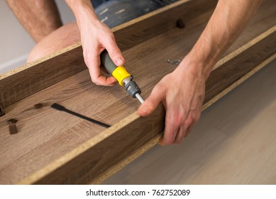 The worker sets a new handle on the white cabinet with a screwdriver - Shutterstock ID 762752089