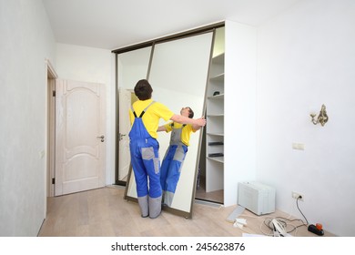 Worker setting mirrored doors on corner sliding wardrobe in room 