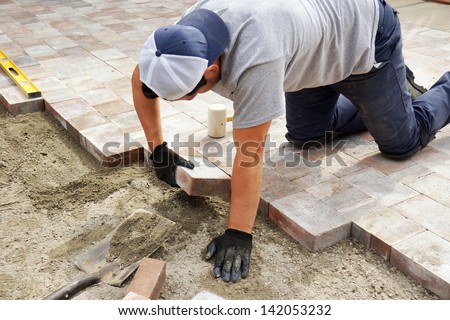 Worker setting paver bricks on large patio, paving backyard