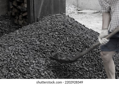 A Worker With A Shovel Unloads Black Coal Against The Background Of A Large Pile Of Coal. Energy Crisis. Soft Focus.